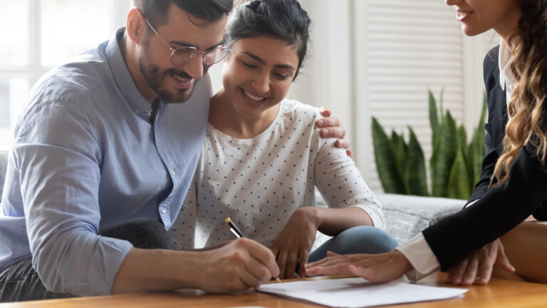 Couple signing paperwork with a smiling advisor at home.