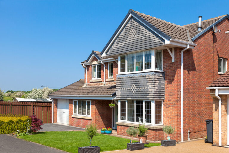 Modern British detached house with garage, front garden, and clear blue sky.