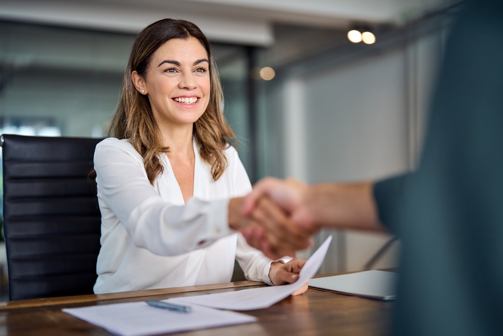 Smiling woman shaking hands at desk during a mortgage consultation in office.