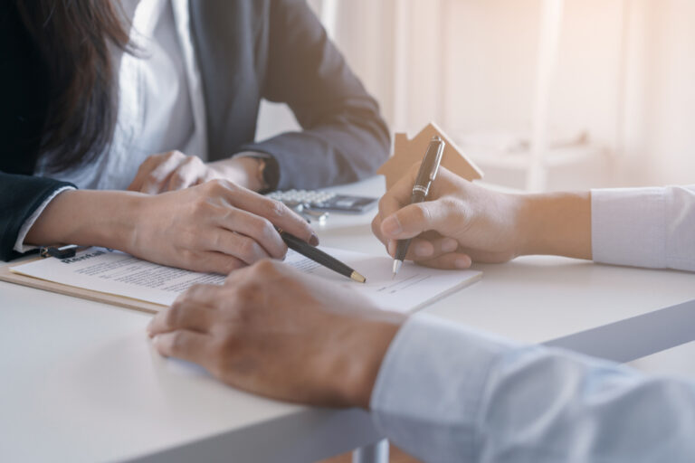 Client signing property agreement with estate agent at desk.