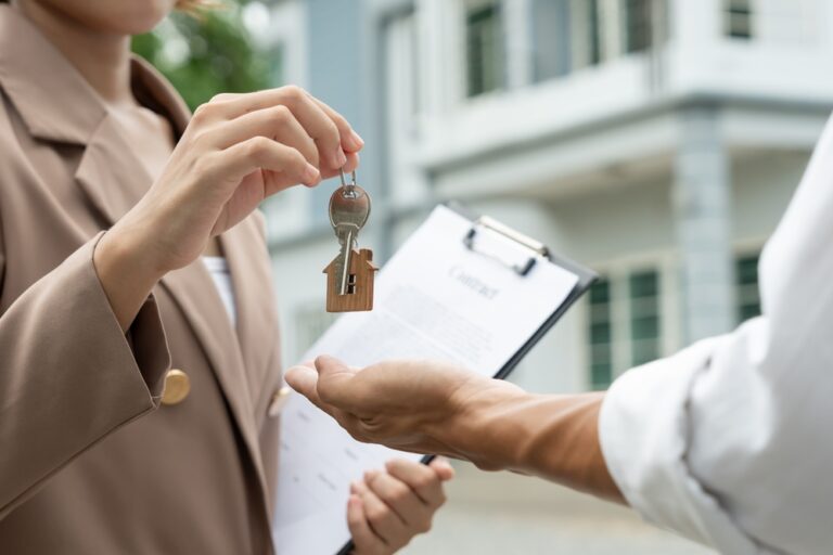 Estate agent handing over house keys with contract in the background.