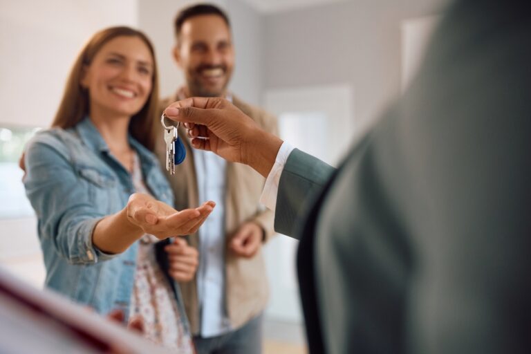 Smiling couple receiving house keys from estate agent in new home.