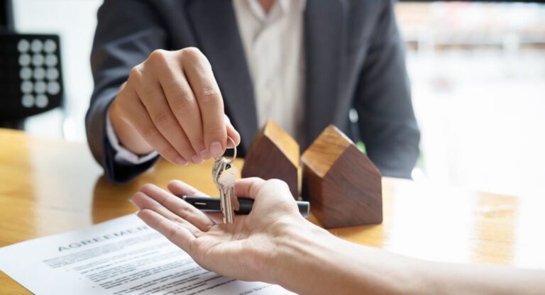 Estate agent handing keys to landlord with property contract on desk