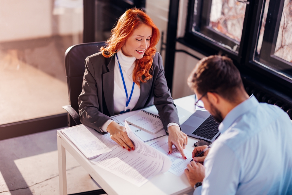 Businesswoman assisting a client with signing documents at a modern office desk.