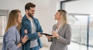 Estate agent smiling and talking with a young couple inside a modern home, representing Whitegates’ tenant retention support and professional property management.