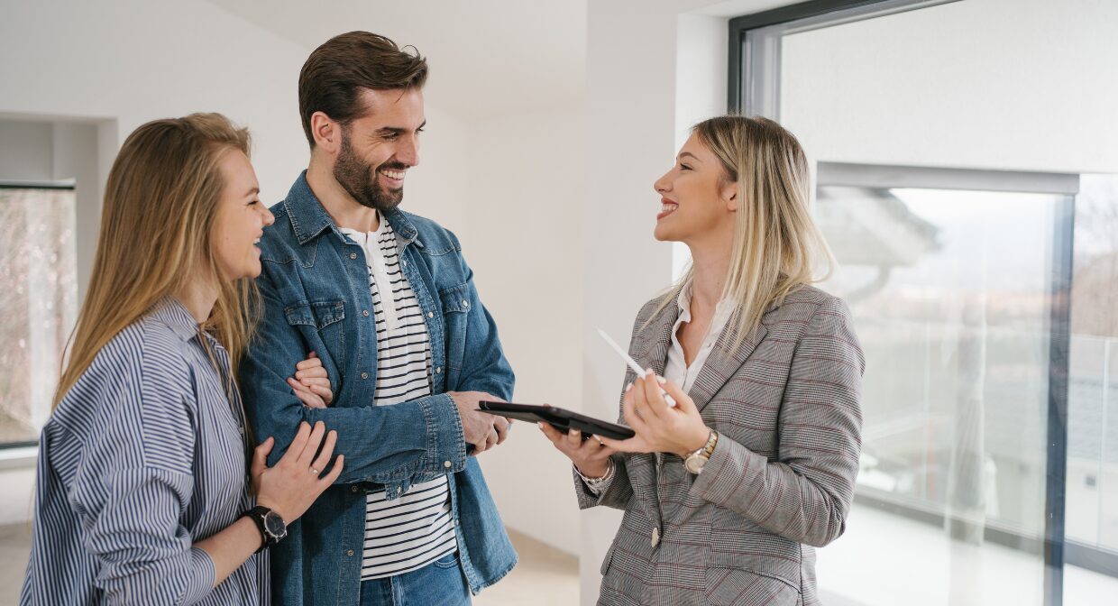Estate agent smiling and talking with a young couple inside a modern home, representing Whitegates’ tenant retention support and professional property management.