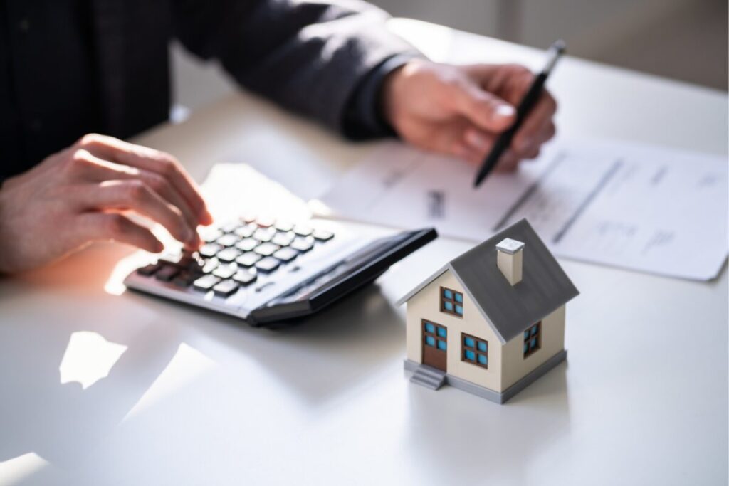 A landlord using a calculator and reviewing property documents beside a small model house, symbolising property management and investment planning.
