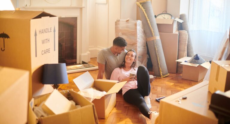 Young couple sitting among moving boxes in their living room while preparing their home for sale and valuation.