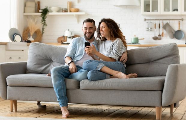 Couple sitting on a couch, looking at a phone.