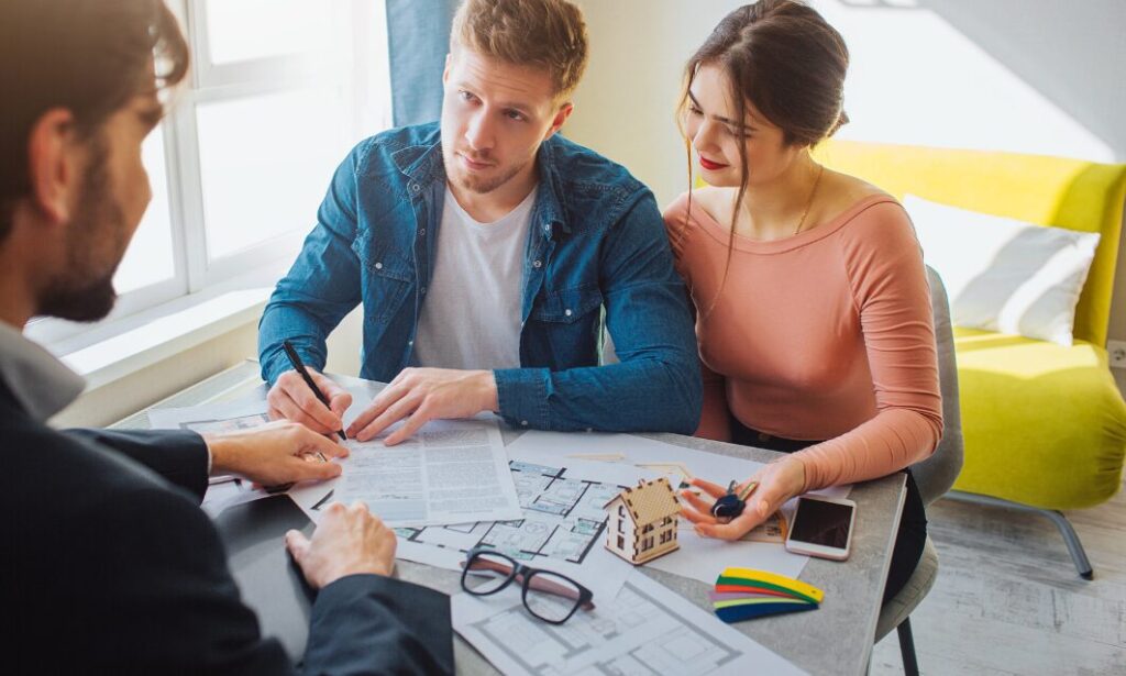 Couple reviewing and signing property documents with a letting agent at a desk.