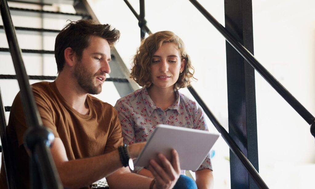 Two people sitting on stairs looking at a digital tablet and discussing tenancy information.