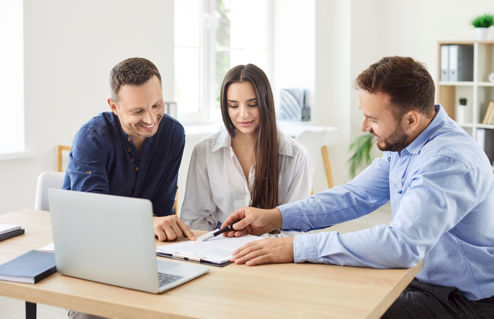 Couple reviewing documents with an adviser at a desk in a bright office