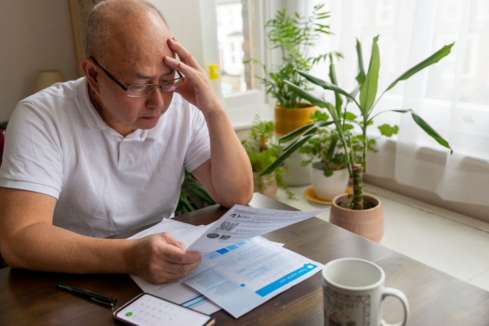 Man reviewing household bills at a table with documents and a smartphone