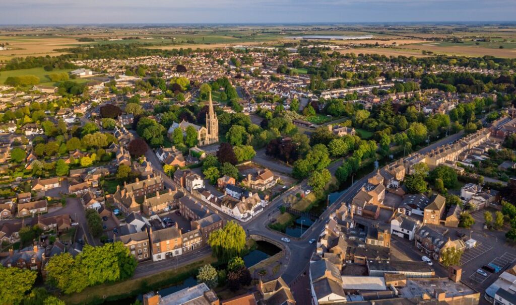 Aerial view of a UK market town with residential streets, green spaces and a church at the centre, showing surrounding homes and countryside
