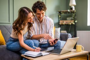 Couple reviewing property details online at home with laptop and phone
