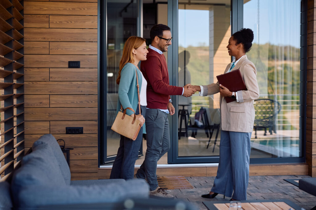 Estate agent shaking hands with couple outside property, representing landlord support and legal compliance in the UK rental market