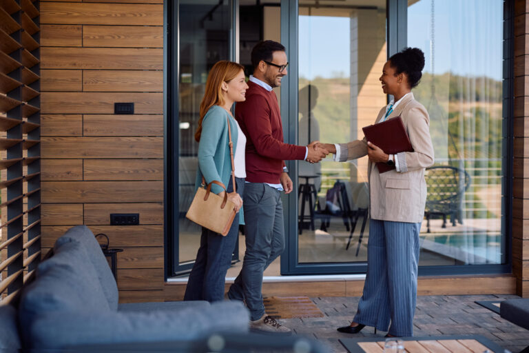 Estate agent shaking hands with couple outside property, representing landlord support and legal compliance in the UK rental market