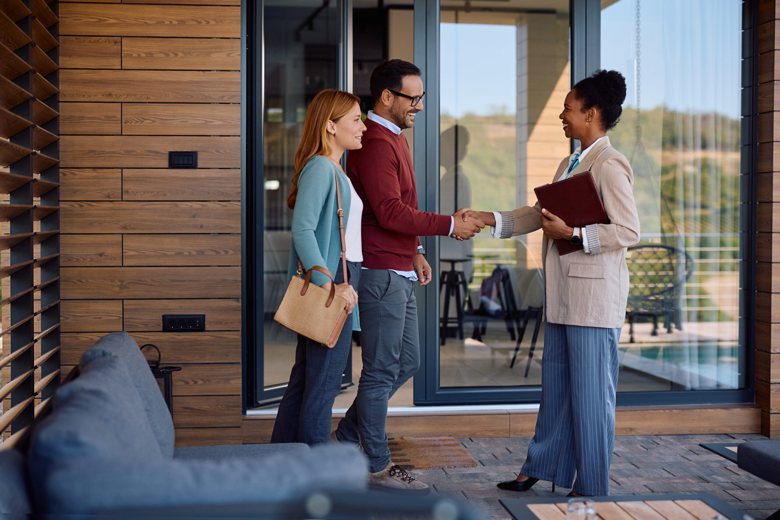 Estate agent shaking hands with couple outside property, representing landlord support and legal compliance in the UK rental market