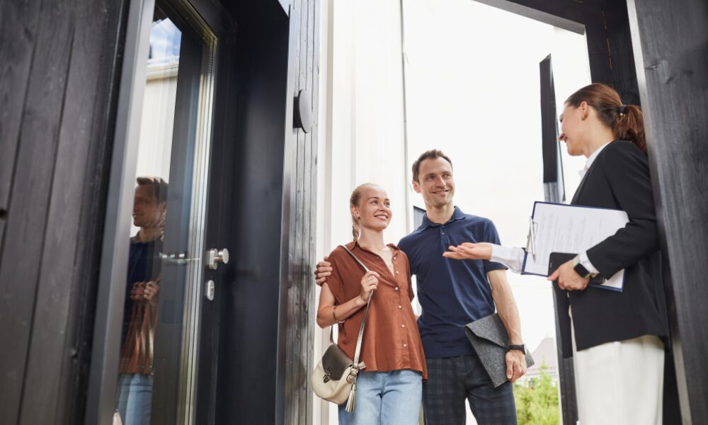 Estate agent discussing rental property details with prospective tenants outside a home related to the Decent Homes Standard private rental rules.