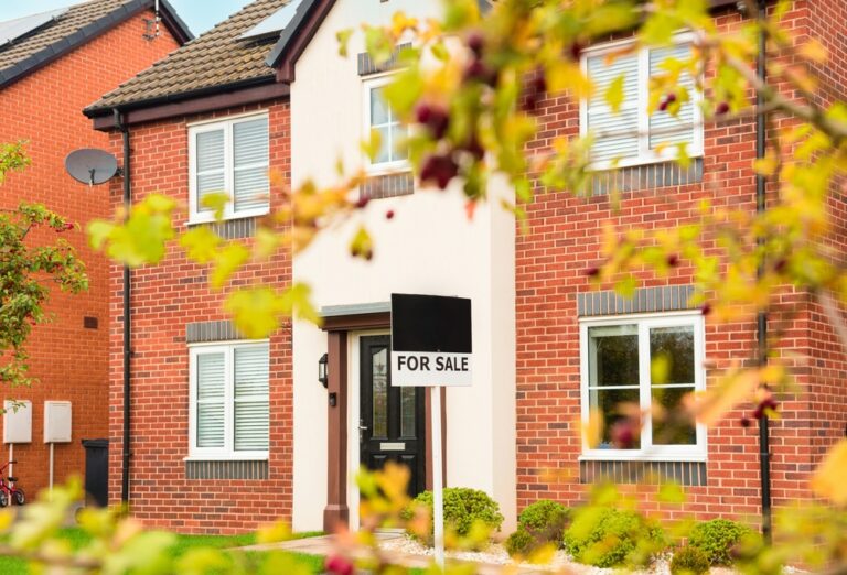 Modern red-brick house with for sale sign in front garden