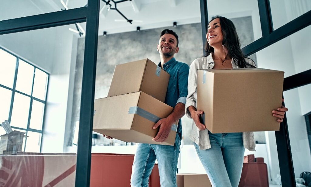 Young couple carrying boxes into their new home, first-time buyers
