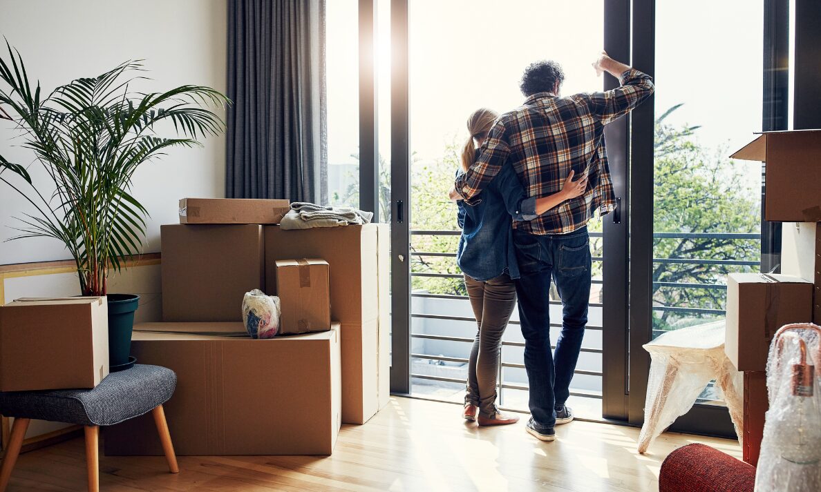 Young couple standing by window in new home surrounded by moving boxes