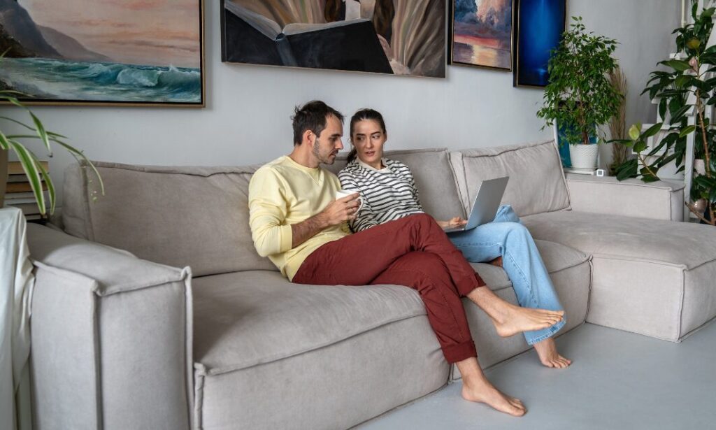 couple sitting on sofa using laptop to research property prices and housing market trends
