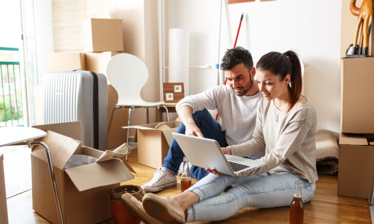 A couple sitting among moving boxes using a laptop while searching for a rental property in Prescot. Focus keyword: