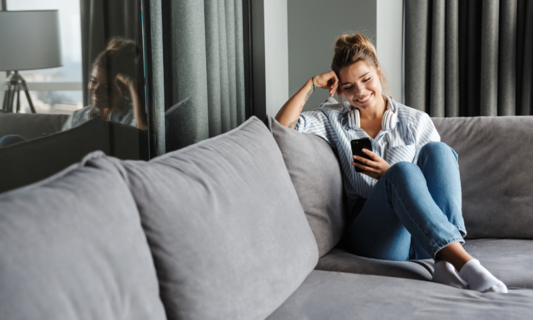 Woman relaxing on a sofa while using her smartphone to search for property online.