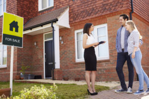 Estate agent showing a couple a house with a for sale sign